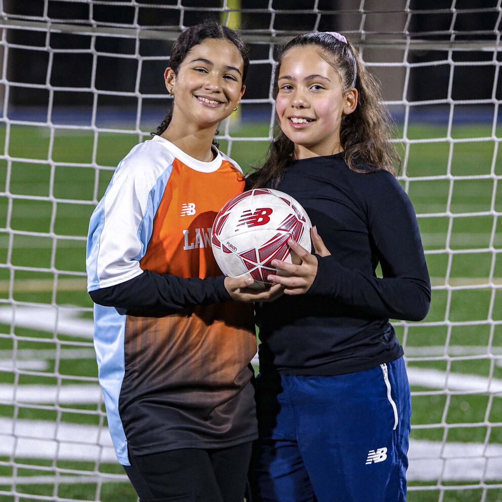 Two young female - presenting child holding football and smiling.